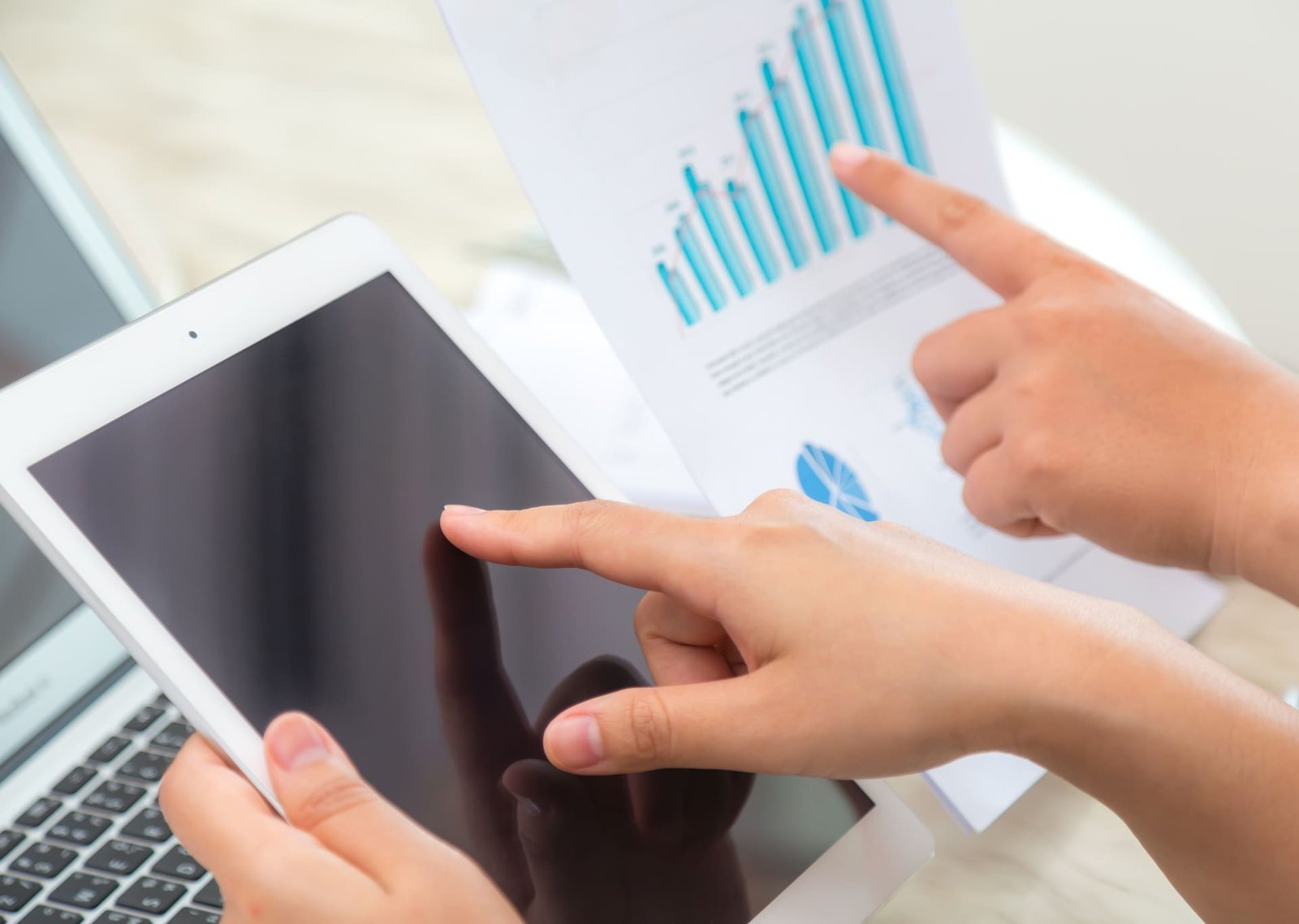 Close-up de duas mãos apontando para um tablet e um gráfico impresso, simbolizando análise de dados e estratégias de SEO realizadas por uma agência especializada em marketing digital para melhorar resultados online.