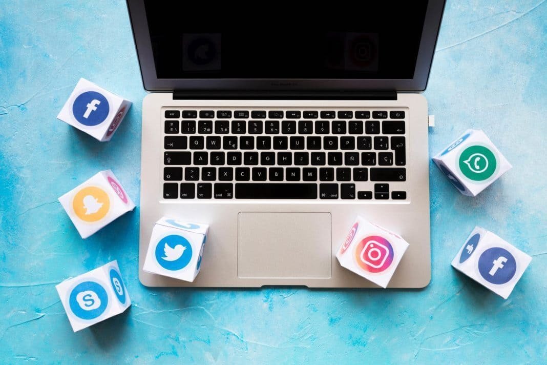 Notebook com ícones de redes sociais como Facebook, Instagram, Twitter e WhatsApp ao redor, representando estratégias para redes sociais com foco em diferenciação digital — Agência Mais Resultado.